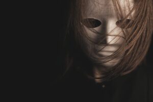 A mysterious figure wearing a mask, partially obscured by hair, in dramatic lighting.