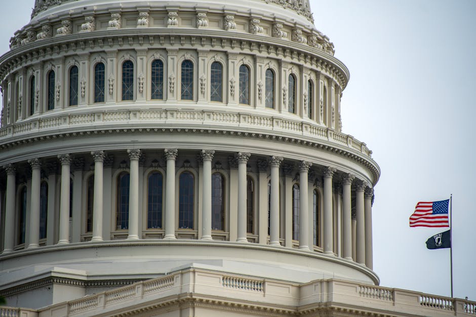Detail of the US Capitol dome in Washington, D.C., featuring an American flag waving beside it.
