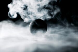 A dark sphere surrounded by swirling white smoke on a black background.