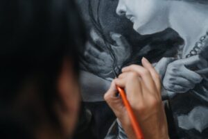 Close-up of artist carefully painting a detailed portrait using fine brushes.