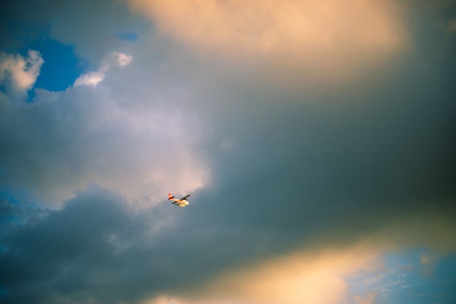 Aerial view of airplane flying beneath dramatic and colorful clouds in the evening sky.