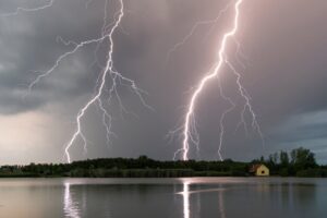 Stunning capture of multiple lightning bolts striking over a calm lake during a thunderstorm at twilight.