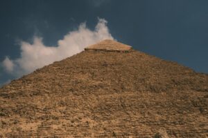 A low-angle view of the majestic Great Pyramid of Giza against a backdrop of clouds and blue sky.