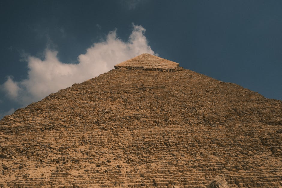 A low-angle view of the majestic Great Pyramid of Giza against a backdrop of clouds and blue sky.